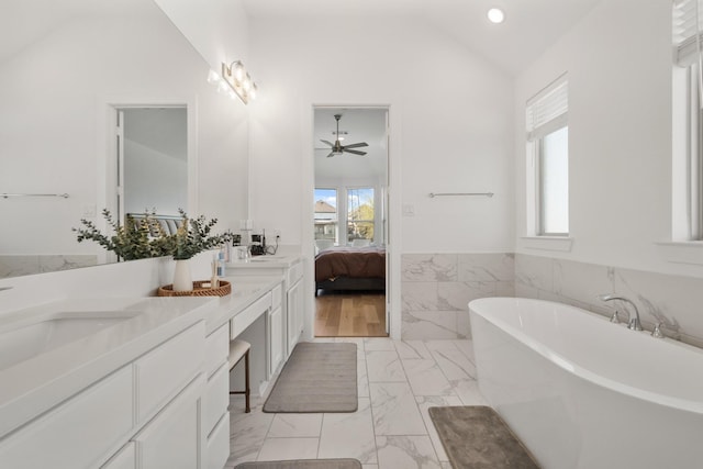 full bath featuring marble finish floor, double vanity, a freestanding bath, vaulted ceiling, and wainscoting