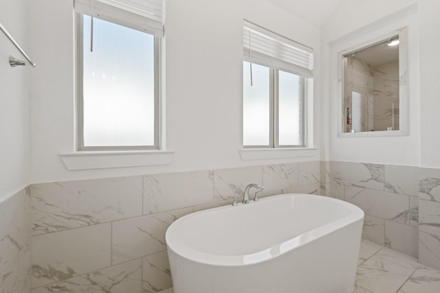 full bath with marble finish floor, a freestanding bath, tile walls, and wainscoting