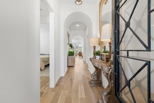 hall with arched walkways, baseboards, and light wood-style floors