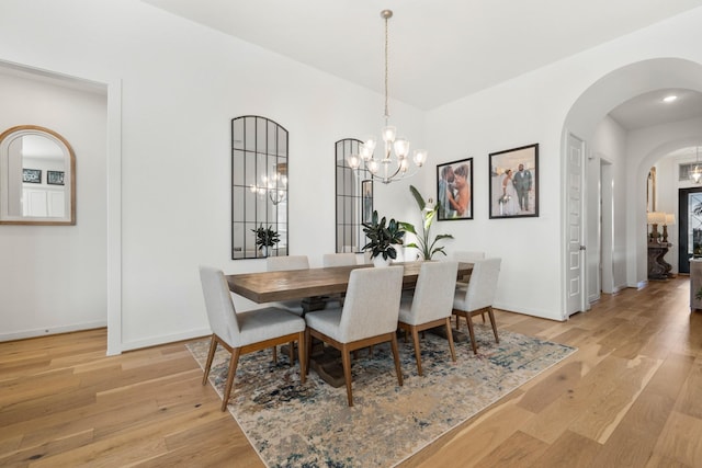 dining room with light wood-style flooring, arched walkways, baseboards, and a chandelier