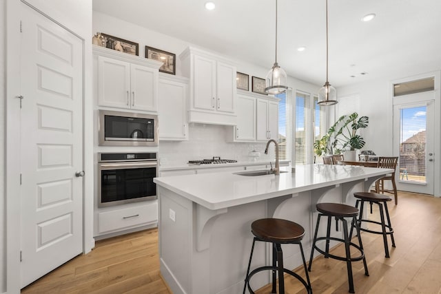 kitchen featuring light countertops, light wood-type flooring, stainless steel appliances, backsplash, and a sink