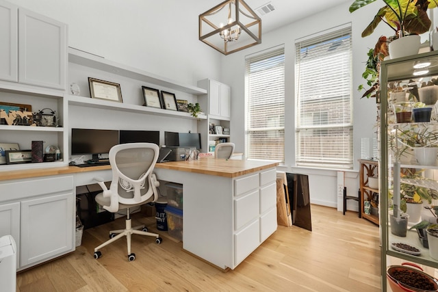 office area featuring light wood finished floors, visible vents, built in desk, and a chandelier