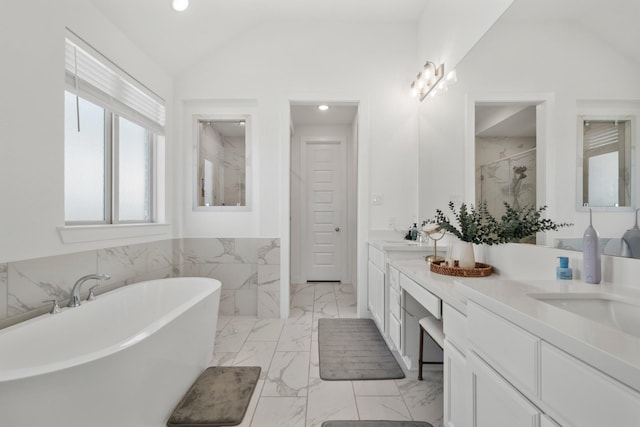 full bath with marble finish floor, vaulted ceiling, a freestanding bath, and double vanity