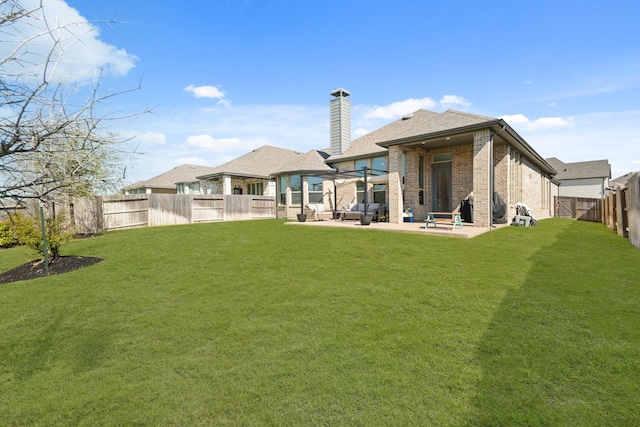 back of property with a patio, a chimney, a fenced backyard, brick siding, and a lawn