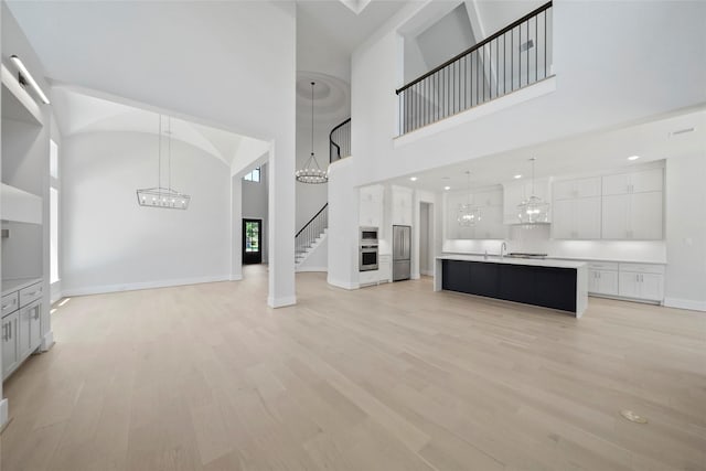 1905 Norcrest Dr, Houston, TX 77055 - unfurnished living room featuring a towering ceiling, a chandelier, light wood-style floors, baseboards, and stairway