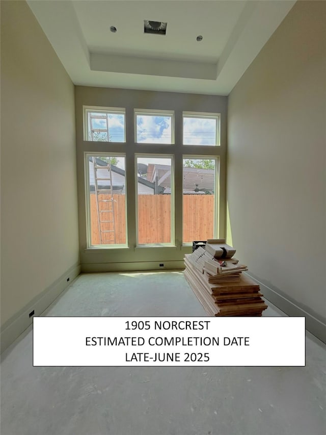 interior space featuring concrete floors, a raised ceiling, and baseboards