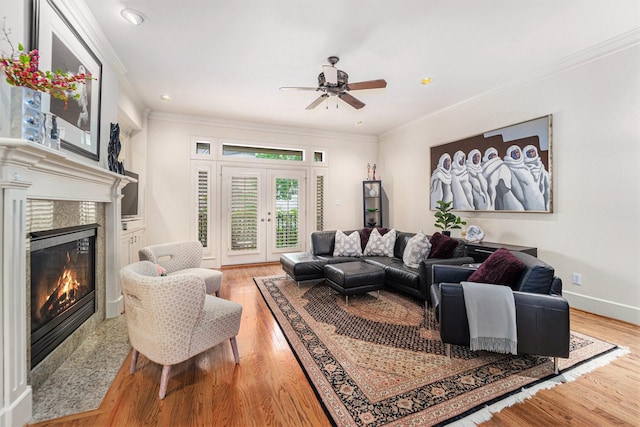 living area with a tile fireplace, ornamental molding, a ceiling fan, and light wood finished floors