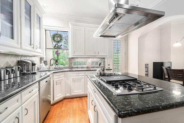 kitchen featuring wall chimney range hood, white cabinetry, crown molding, stainless steel appliances, and a sink