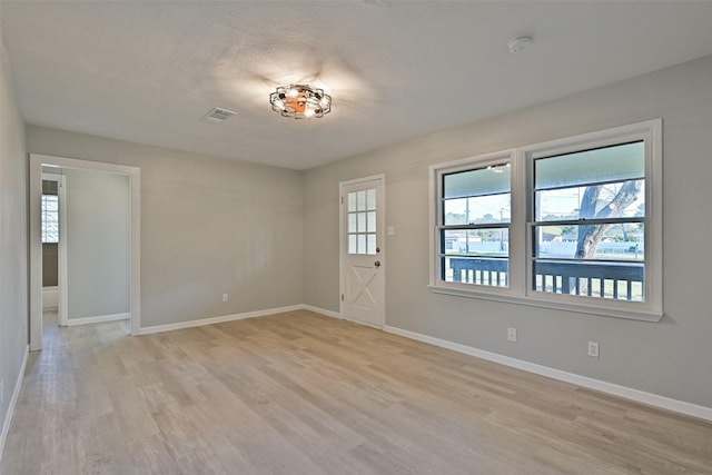 spare room with baseboards, light wood-style flooring, and visible vents