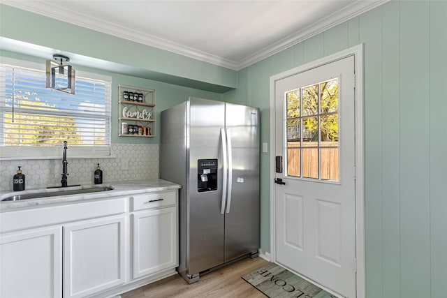 kitchen with light wood-style flooring, ornamental molding, stainless steel fridge with ice dispenser, a sink, and white cabinets