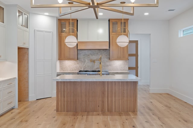 kitchen with light countertops, light wood-style floors, decorative backsplash, and a kitchen island with sink