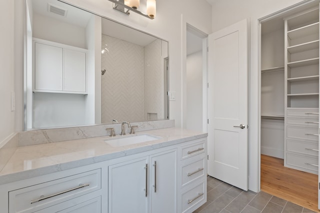 bathroom with a walk in closet, vanity, tile patterned floors, and visible vents