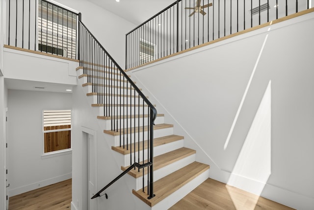 stairway with wood finished floors, a healthy amount of sunlight, a towering ceiling, and baseboards