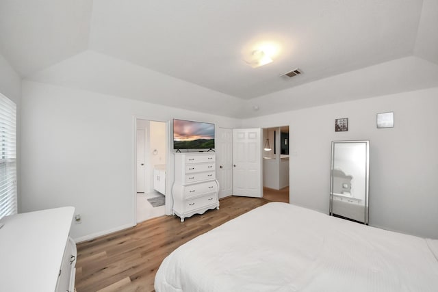 bedroom featuring vaulted ceiling, a raised ceiling, wood finished floors, ensuite bathroom, and visible vents