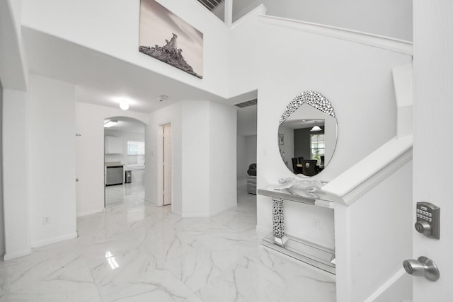 hallway with a high ceiling, marble finish floor, baseboards, visible vents, and arched walkways
