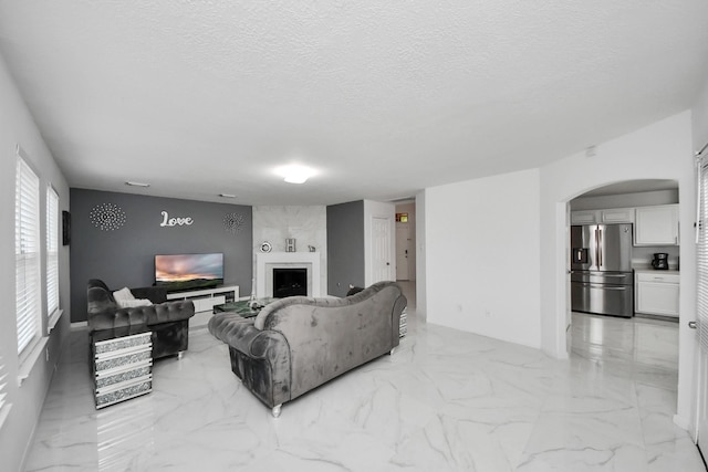 living room with arched walkways, marble finish floor, a textured ceiling, and a fireplace