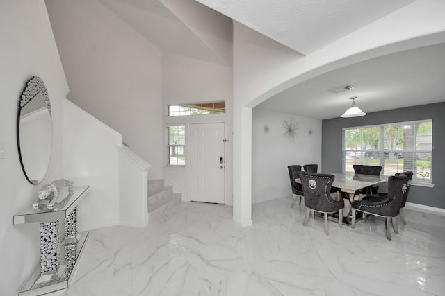 dining space featuring marble finish floor, arched walkways, a healthy amount of sunlight, and stairs