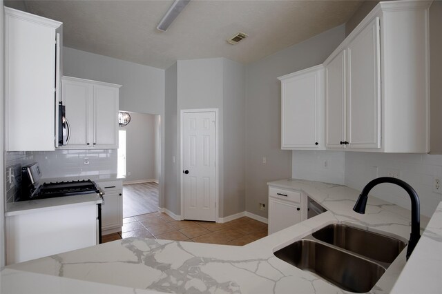 kitchen featuring tasteful backsplash, light tile patterned floors, light stone counters, a sink, and stainless steel appliances