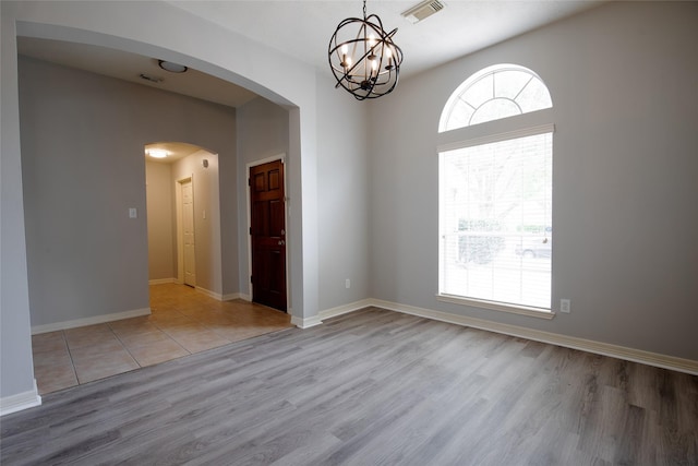 spare room with visible vents, arched walkways, wood finished floors, and an inviting chandelier