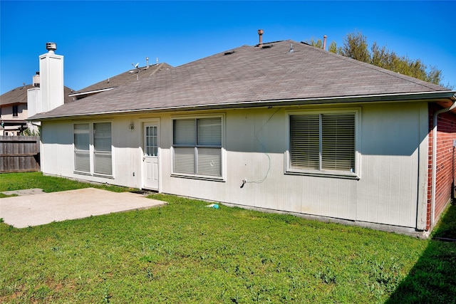 back of house featuring fence, roof with shingles, a chimney, a patio area, and a lawn