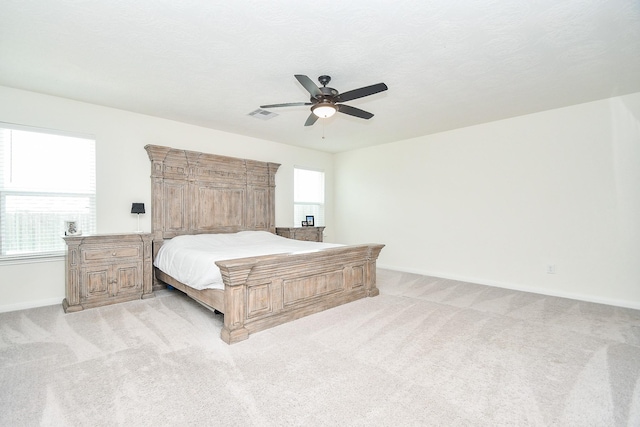 bedroom with a textured ceiling, baseboards, light colored carpet, visible vents, and ceiling fan