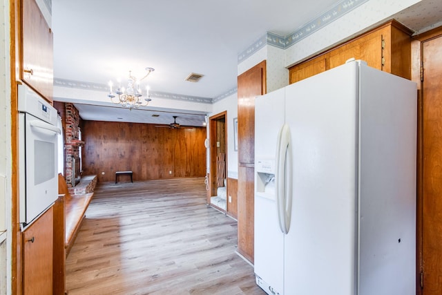 kitchen with white appliances, brown cabinetry, light wood-style floors, and a chandelier