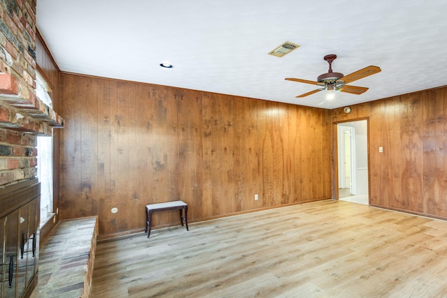 spare room with visible vents, wood finished floors, wood walls, and a ceiling fan