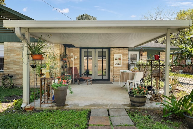 doorway to property featuring brick siding, fence, and french doors