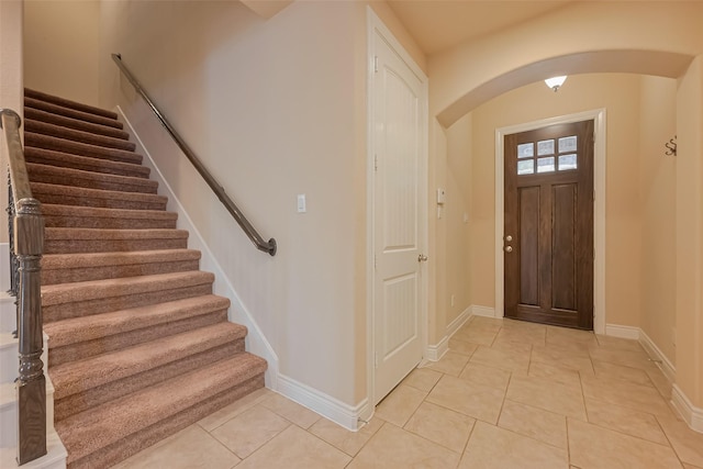 entryway featuring light tile patterned floors, baseboards, arched walkways, and stairs