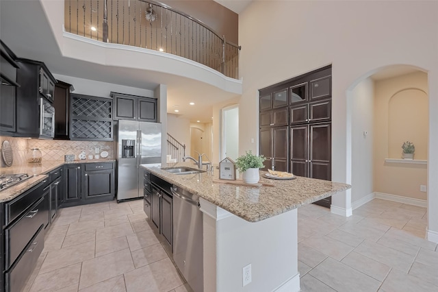 kitchen with tasteful backsplash, light stone countertops, a center island with sink, stainless steel appliances, and a sink