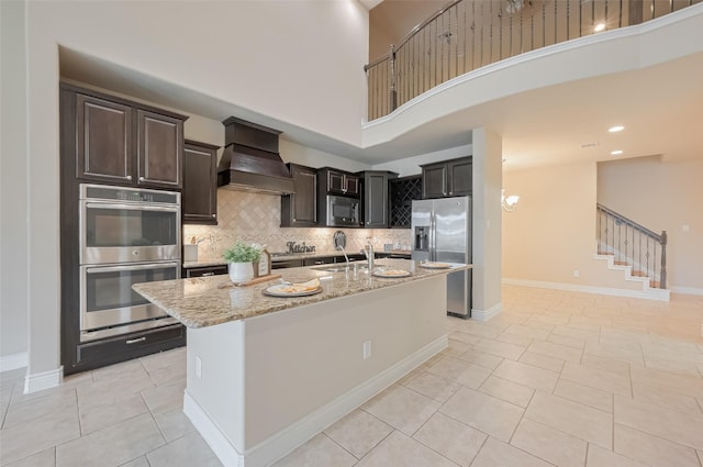 kitchen with light stone countertops, custom exhaust hood, stainless steel appliances, decorative backsplash, and baseboards