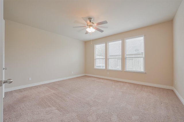 empty room with light colored carpet, baseboards, and a ceiling fan