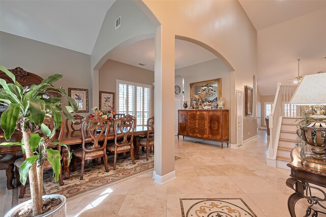 interior space featuring arched walkways, high vaulted ceiling, visible vents, and baseboards