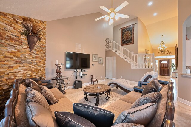 tiled living area with arched walkways, high vaulted ceiling, ceiling fan with notable chandelier, baseboards, and stairway