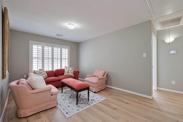 living area featuring baseboards, attic access, light wood finished floors, and visible vents