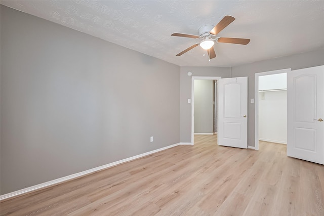 unfurnished bedroom featuring a closet, light wood-style floors, baseboards, ceiling fan, and a spacious closet
