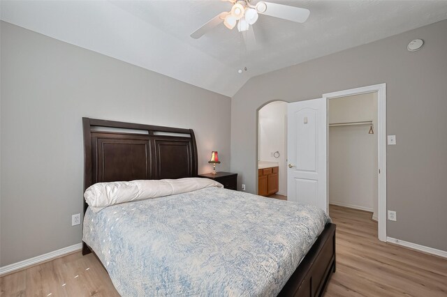 bedroom with ceiling fan, ensuite bath, baseboards, light wood-type flooring, and vaulted ceiling