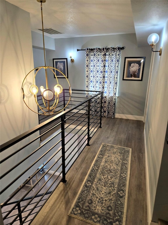 corridor featuring a chandelier, an upstairs landing, wood finished floors, and baseboards