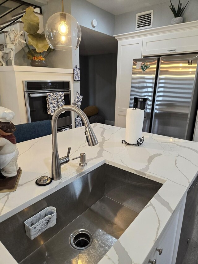 kitchen featuring stainless steel fridge, a sink, oven, white cabinets, and light stone counters