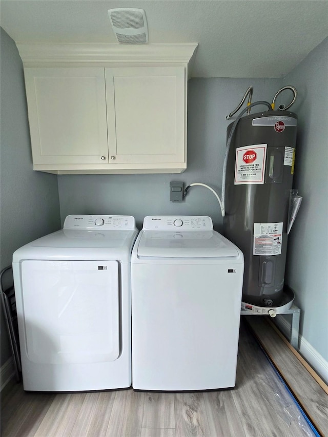 clothes washing area with water heater, washing machine and dryer, light wood finished floors, and cabinet space