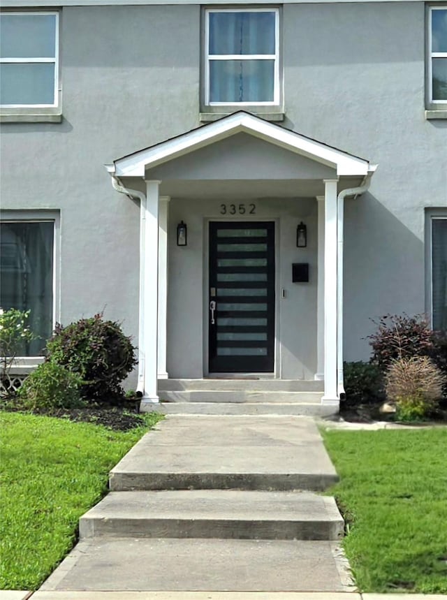view of exterior entry featuring stucco siding and a lawn