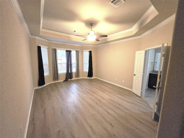 empty room with a raised ceiling, crown molding, wood finished floors, ceiling fan, and baseboards