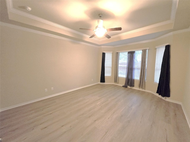 spare room featuring a tray ceiling, wood finished floors, crown molding, a ceiling fan, and baseboards