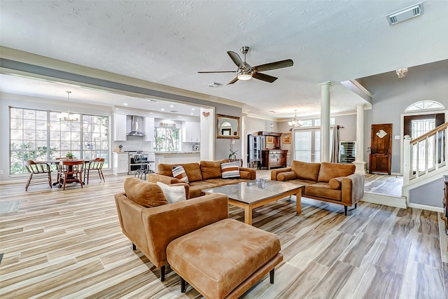 living area with visible vents, light wood-type flooring, decorative columns, and ceiling fan with notable chandelier
