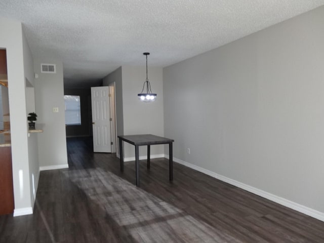 unfurnished dining area with a textured ceiling, baseboards, dark wood-style floors, and visible vents