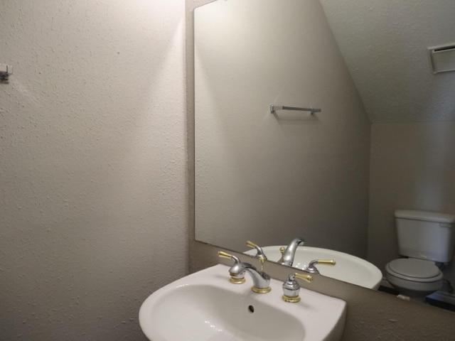 half bath featuring lofted ceiling, a textured ceiling, a sink, and toilet
