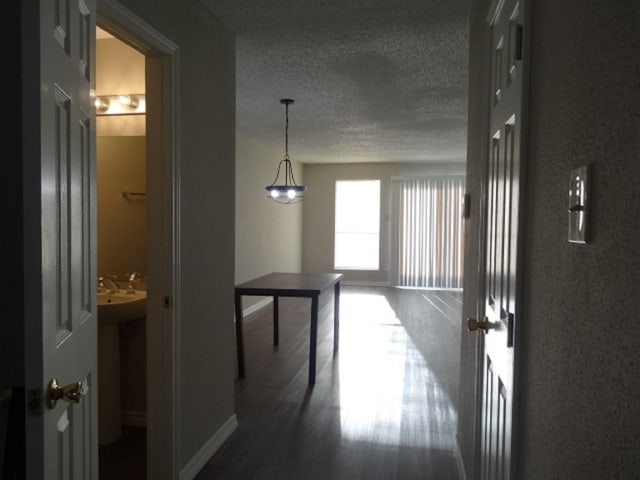 hall featuring baseboards, a textured ceiling, and wood finished floors