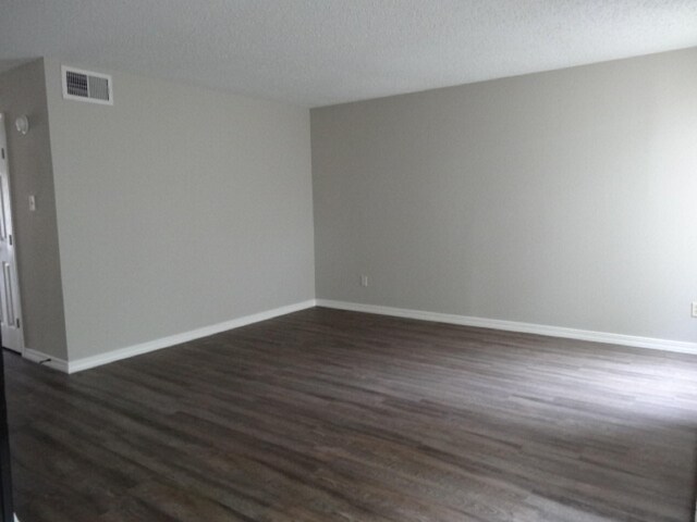 spare room with dark wood-type flooring, baseboards, a textured ceiling, and visible vents
