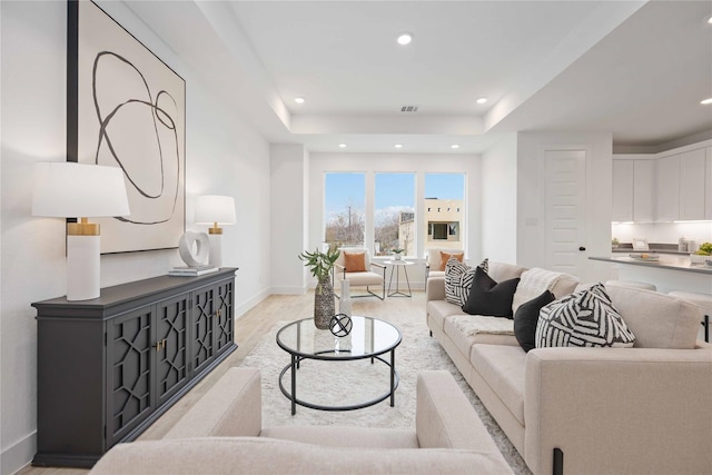living room featuring visible vents, baseboards, recessed lighting, a raised ceiling, and light wood-style floors