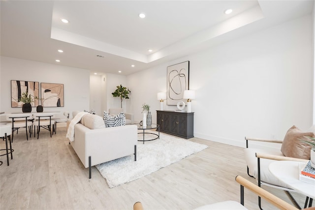 living area featuring a raised ceiling, baseboards, light wood-style flooring, and recessed lighting
